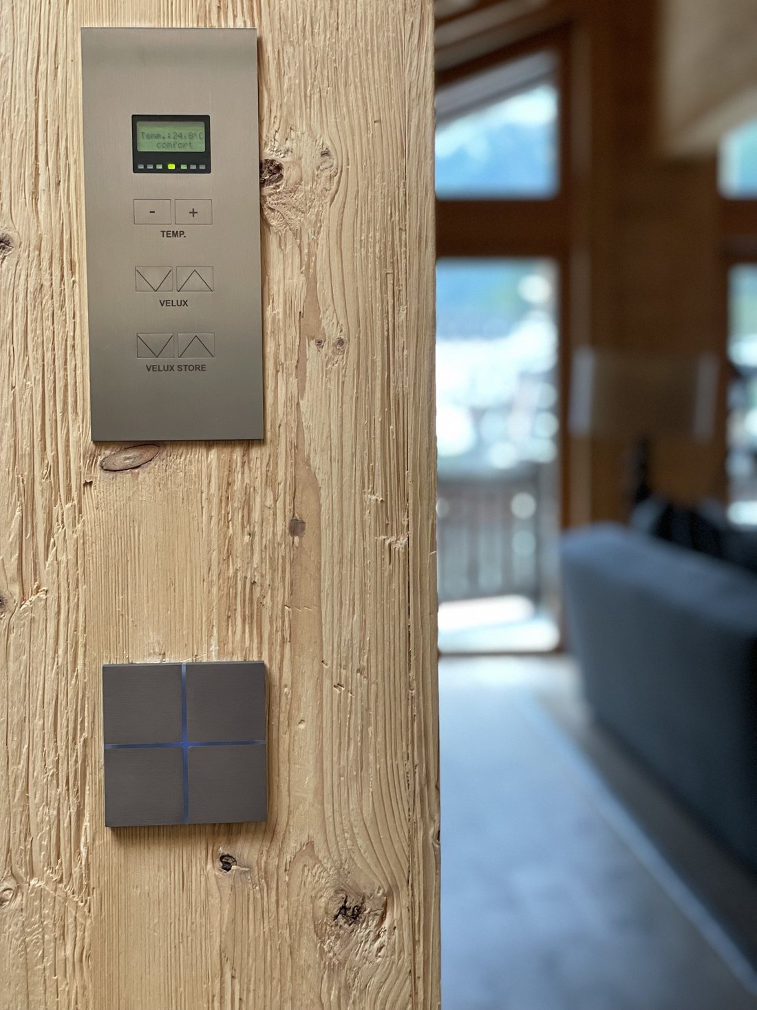Brushed-metal climate panel and KNX keypad on the aged timber of a chalet