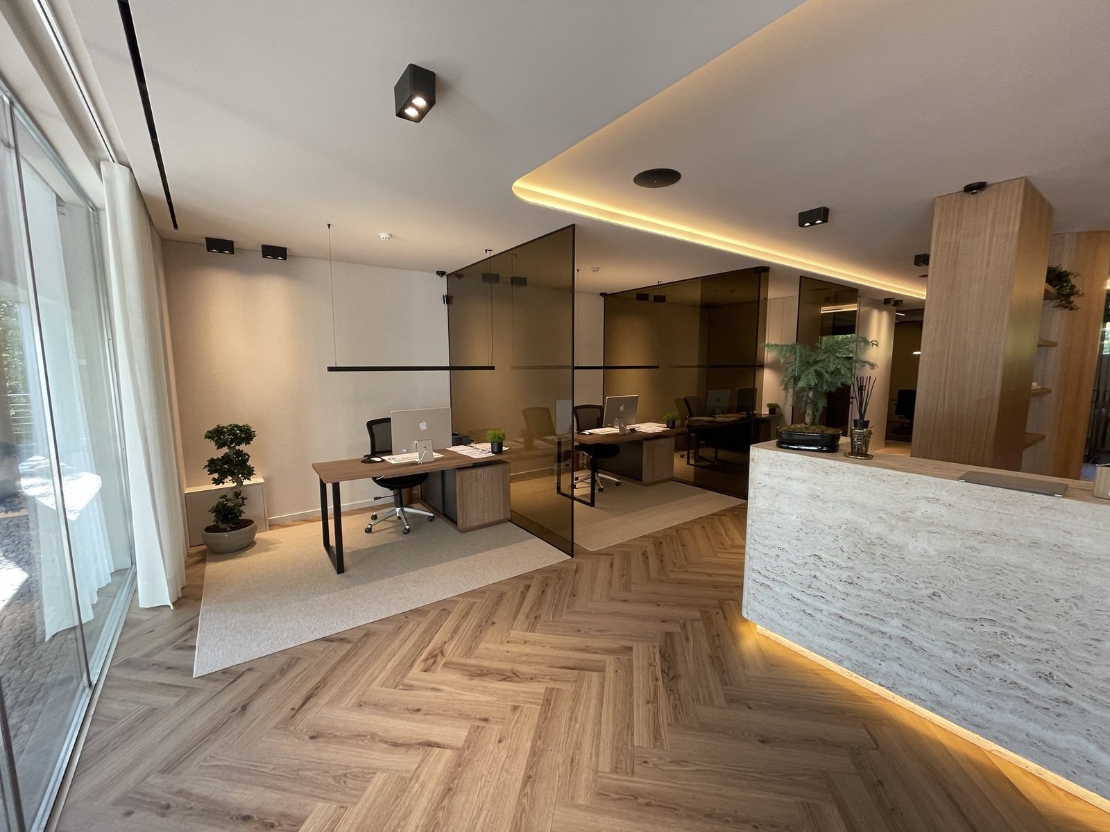 Office with a lit ceiling cove, travertine reception desk with grazing light and smoked-glass partitions